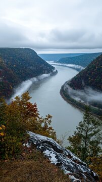 Un fleuve sinueux serpente &agrave; travers des collines bois&eacute;es brumeuses sous un ciel couvert