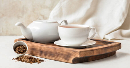 Wooden board with cup of tasty hojicha green tea and pot on table