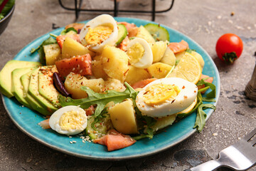 Plate of tasty potato salad with eggs and avocado on grey background