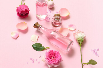 Bottles of cosmetic oil with rose extract and flowers on pink background