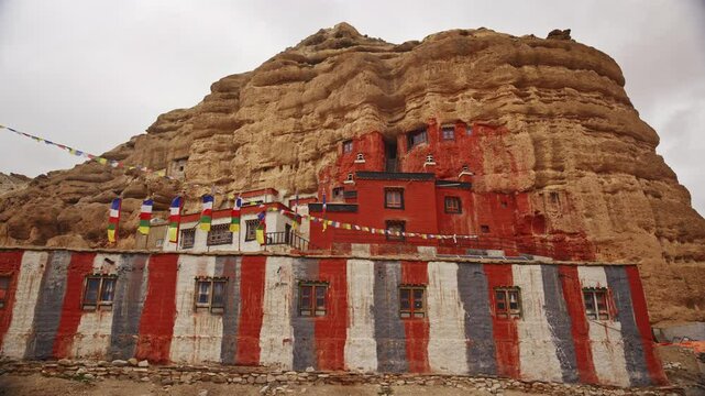Sacred Sun Cave Monastery Nestled In Mustang's Cliff With Colorful Prayer Flags