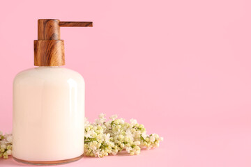 Soap dispenser with white lilac twig on pink background