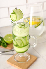 Glass and jug of infused water with cucumber slices on grey tile table