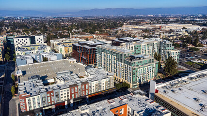 Fototapeta premium Aerial view of modern mixed-use development in downtown Sunnyvale, California. Residential and commercial buildings against mountain backdrop