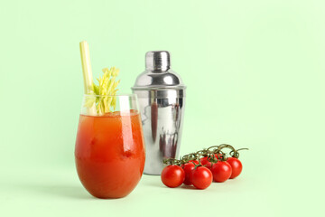 Glass of bloody mary with celery and shaker on green background