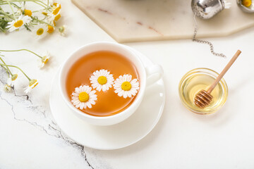 Cup of hot chamomile tea and honey on white marble background