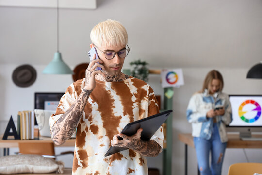 Male graphic designer with tablet talking by mobile phone in office