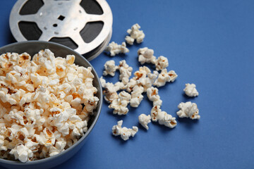 Bowl with tasty popcorn and film reel on blue background
