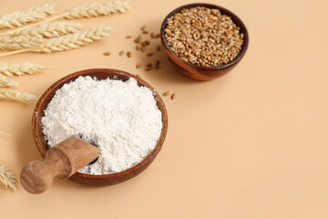 Bowls with wheat flour and grains on beige background