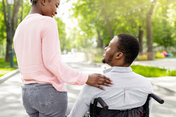 Young black woman and her disabled boyfriend in wheelchair spending time together outdoors, back...