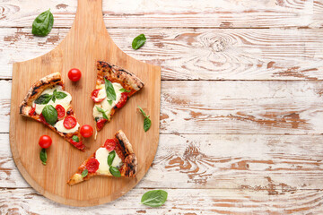 Board with slices of tasty pizza Margarita and fresh tomatoes on light wooden background