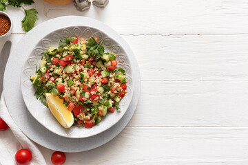 Plate with delicious tabbouleh salad on light wooden background
