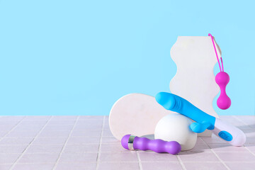 Decorative stands with different sex toys on pink tile near blue wall