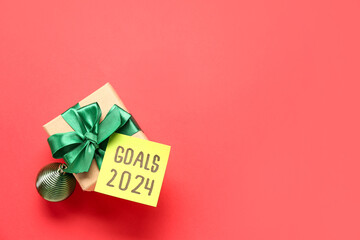 Sticky note with goals for 2024 and gift box on red background