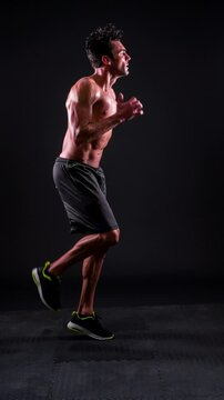 Athletic man working out in front of a black background with dramatic lighting. Slow Motion. Vertical Video.