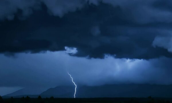 Storm clouds gathering with lightning striking the horizon, ominous scene, concept for climate unpredictability