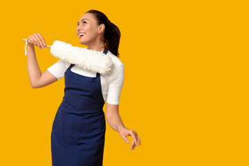 Portrait of happy young housewife in apron with pp duster on yellow background