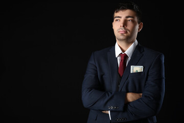 Young businessman with bribe in pocket on dark background