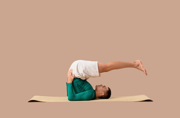 Young man doing yoga on mat against brown background