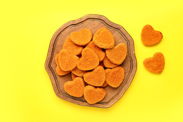 Wooden board with tasty nuggets in shape of heart on yellow background. Valentine's Day celebration