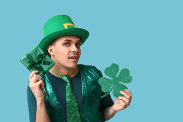 Young man in green clothes, with gift and shamrock on blue background. St. Patrick's Day