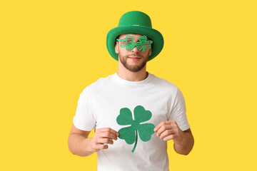 Young man in leprechaun hat and decorative glasses with clover on yellow background. St. Patrick's...