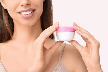 Beautiful young woman with jar of face cream on pink background