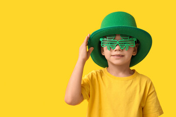 Cute little boy in leprechaun hat and decorative glasses in shape of clover on yellow background....