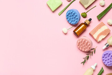 Hair scalp massagers with shampoo bars, bottles of cosmetic products and flowers on pink background