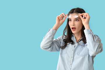 Surprised young woman putting off eyeglasses on blue background