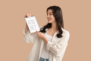 Happy smiling young woman holding notebook with text KETO DIET on beige background
