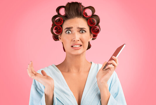 Oops. Confused Housewife Holding Cellphone Making Helpless Gesture Posing Over Yellow Background. Studio Shot