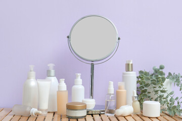Different cosmetic products, mirror and plant on table against color wall