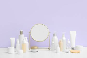 Different cosmetic products and mirror on light table against lilac background