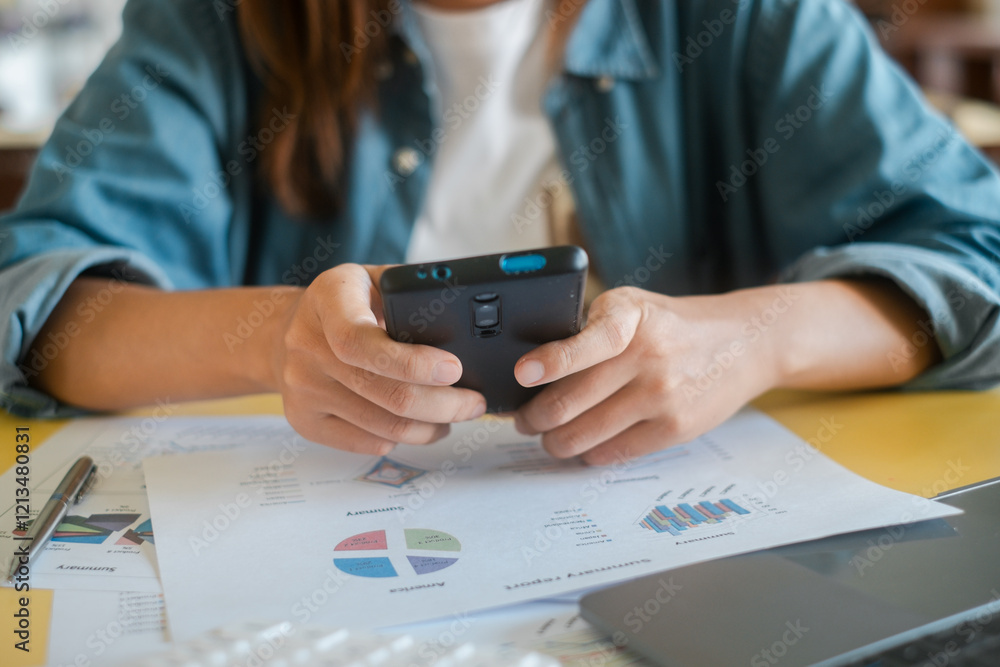 Poster close-up of hands using smartphone over financial documents with charts and graphs, showcasing busin
