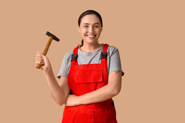 Young female construction worker with hammer on beige background. Woman in male profession concept