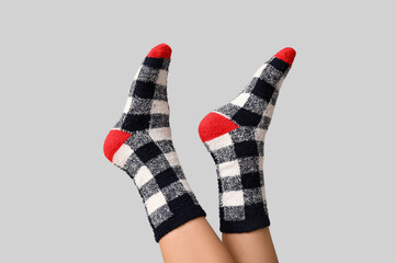 Legs of young woman in warm checkered socks on grey background