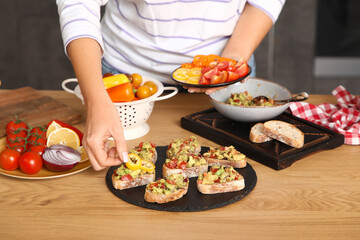 Young woman cooking vegan bruschettas at table in kitchen, closeup
