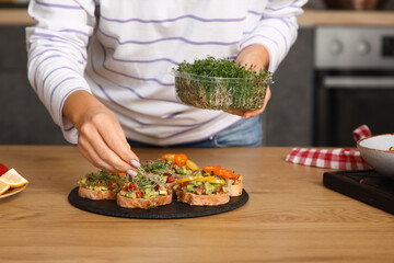 Young woman with micro green cooking vegan bruschettas at table in kitchen, closeup