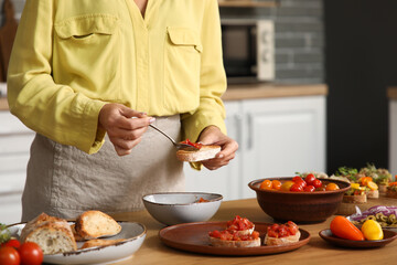 Young woman cooking tasty vegan bruschetta at table in kitchen, closeup