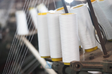 The production of spools of thread occurs in a textile factory setting