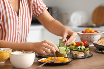 Woman with cucumber cooking vegan bruschettas at table in kitchen, closeup