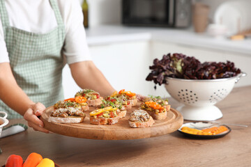 Woman holding board with tasty vegan bruschettas at table in kitchen, closeup