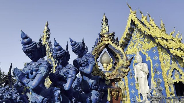 The Blue Temple (Wat Rong Suea Ten) features intricate blue sculptures of deities in prayer, with golden accents and a serene white Buddha in the background, symbolizing peace and devotion.