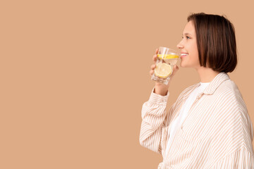 Pretty young woman drinking infused water on beige background