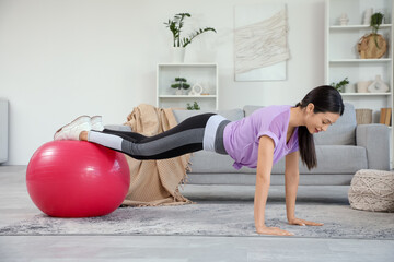 Sporty young woman doing exercises with fitness ball at home