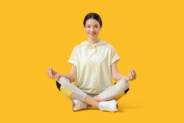 Sporty young woman meditating in lotus position on yellow background