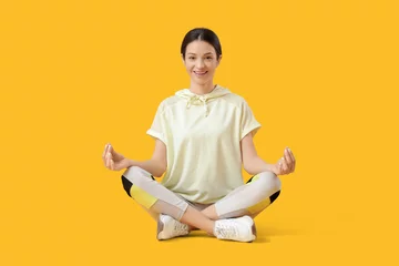 Selbstklebende Fototapeten Sporty young woman meditating in lotus position on yellow background © Pixel-Shot