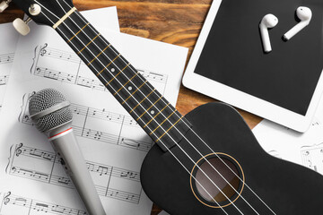 Fototapeta premium Ukulele, microphone, tablet computer, earphones and music sheets on wooden background, closeup