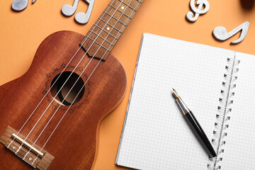 Ukulele, blank notebook, pen and music notes on color background, closeup